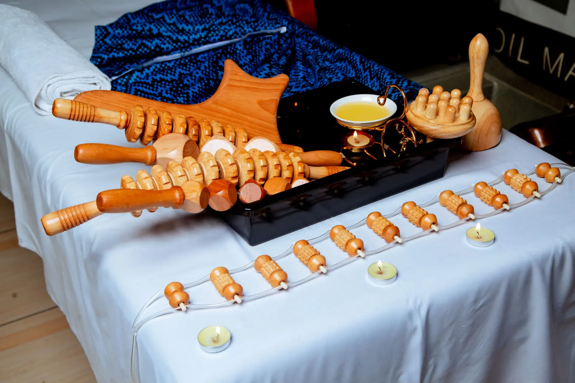 Wooden massage tools, warm oil and tealight candles laid out on a treatment bed